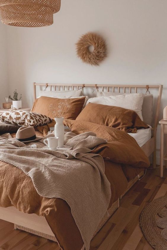 an earthy bedroom in boho style, with wooden furniture, terracotta bedding, a wicker lamp and a wreath of wheat