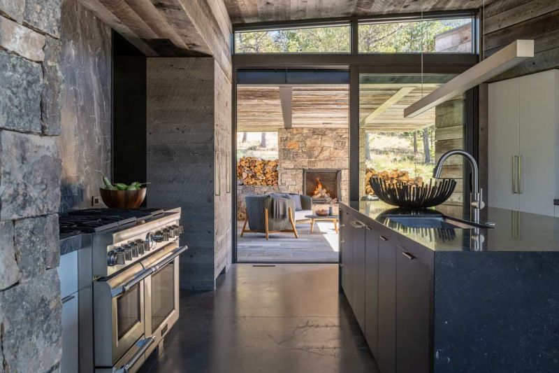 The kitchen features rustic wooden cabinetry, a dark kitchen island and a stone backsplash, there's an access to a covered patio