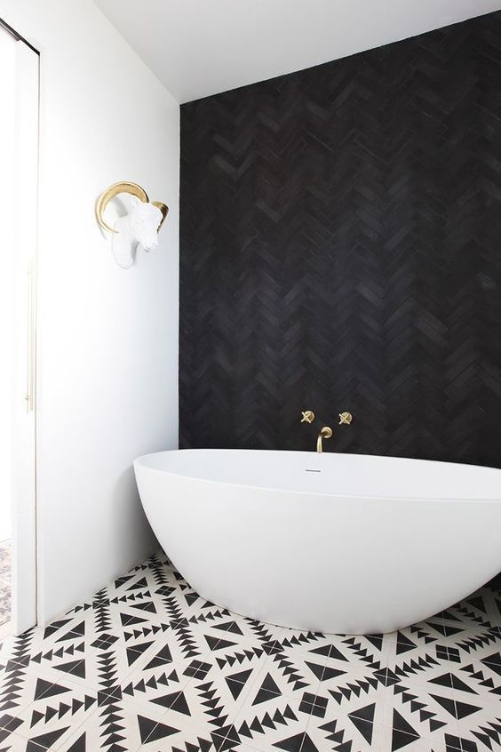 a jaw-dropping bathroom with a black herringbone tile wall, geometric printed tiles and a cool oval bathtub