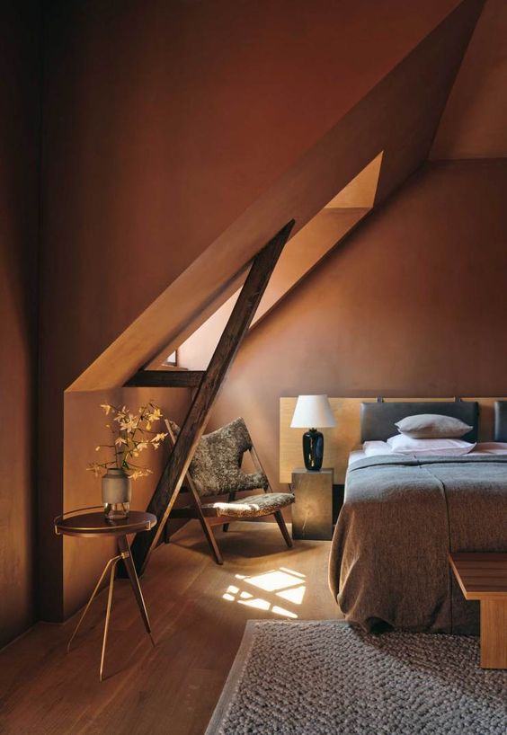 a moody earthy toned bedroom with terracotta walls, wooden furniture, grey and white bedding and gold touches