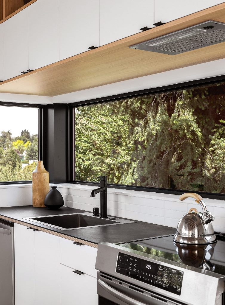 The kitchen is done in white, with black countertops and windows as backsplashes