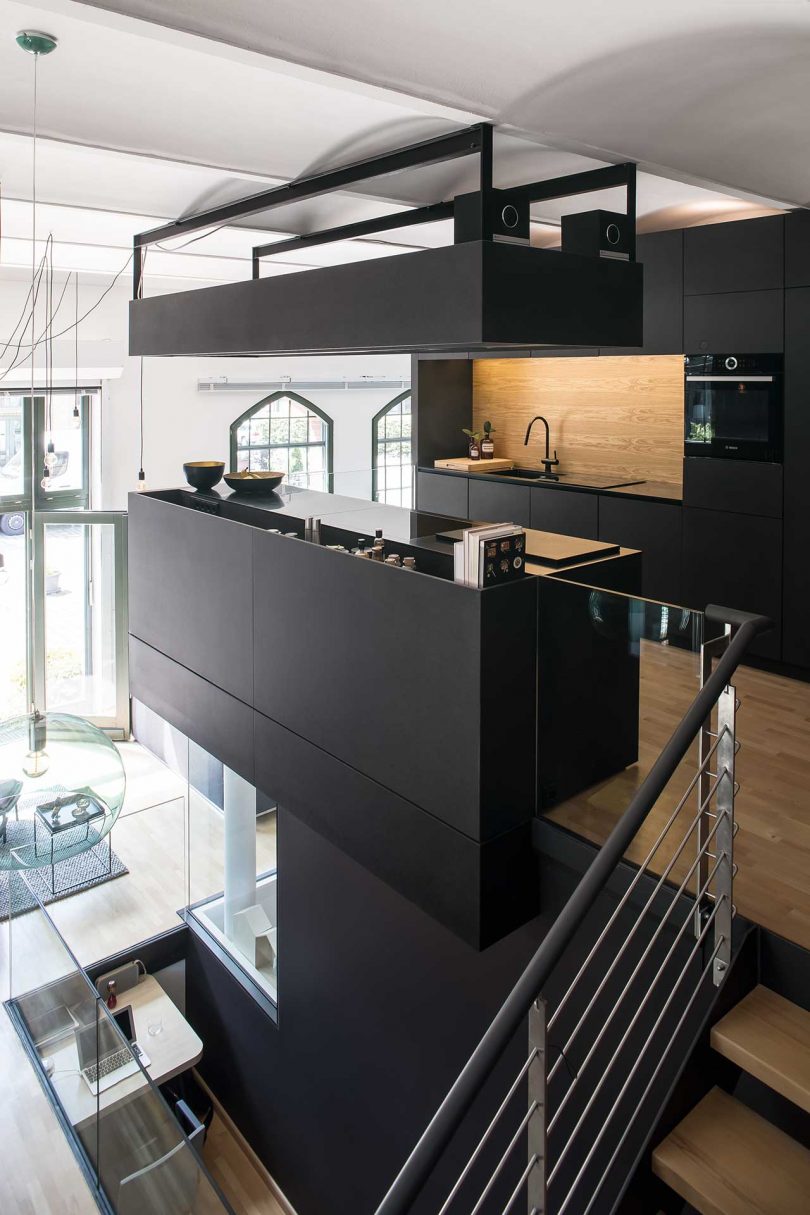 The kitchen upstairs is a super minimalist space done with sleek black cabinetry, with a light colored wooden backsplash and a kitchen island that makes it more comfortable to use