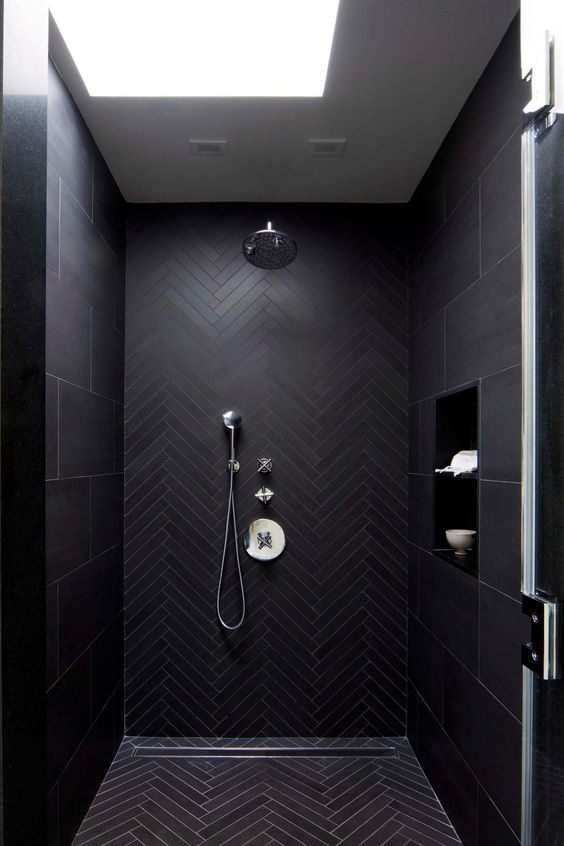 a contemporary moody black bathroom with herringbone and large scale tiles and a skylight to refresh the space