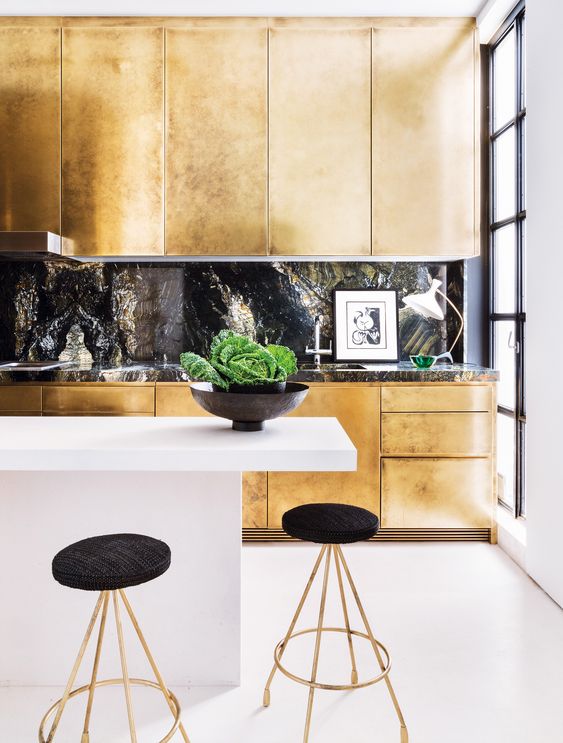A gold kitchen with a black stone backsplash and a countertop plus a white minimalist kitchen island for a jaw dropping look