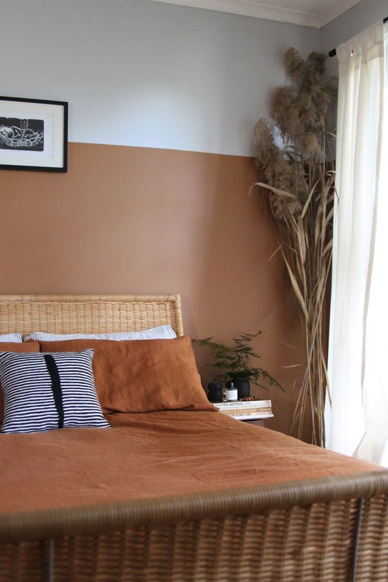 an earthy tone bedroom with a terracotta color block wall, a rattan bed, grasses and potted greenery