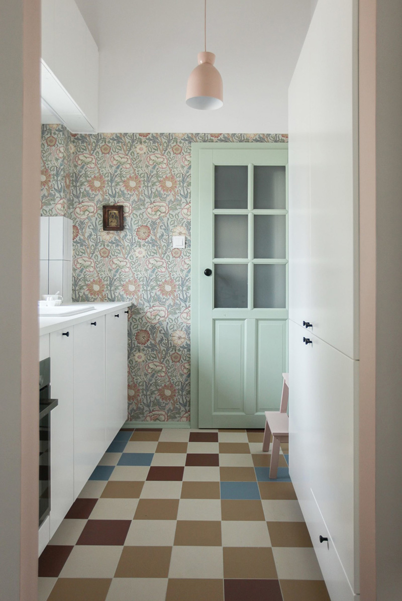06 There’s a small kitchen with Scandinavian wallpaper and white cabinetry, colorful tiles on the floor