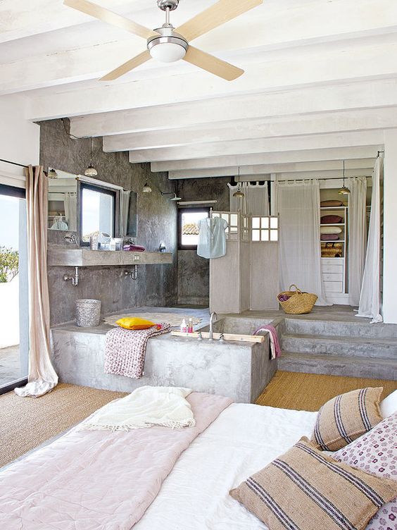 a bedroom combined with a closet and a bathroom clad in concrete, with neutral textiles and printed ones
