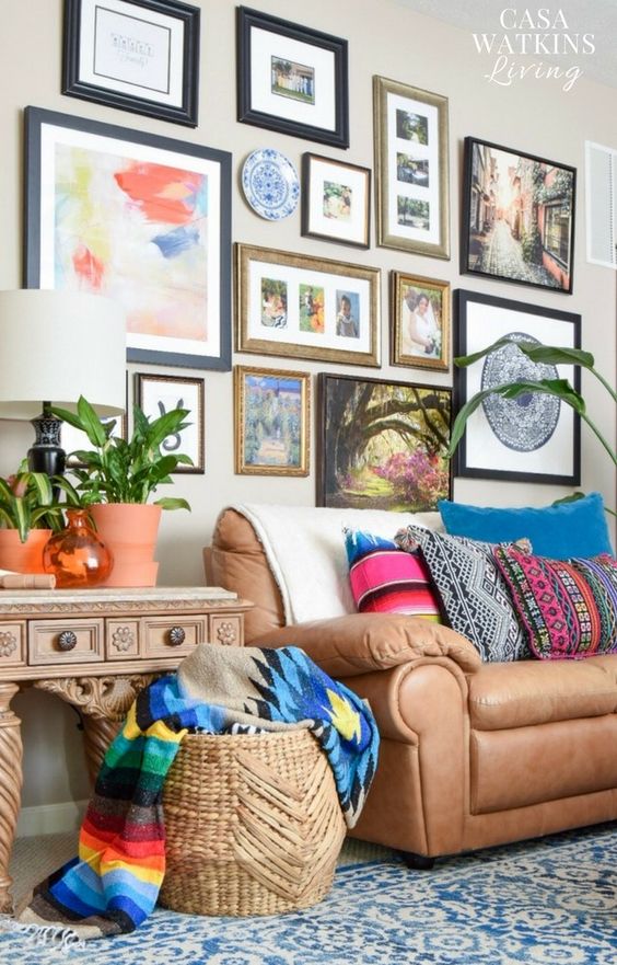 a global eclectic living room with a brown leather sofa, a gallery wall with pretty art, a basket with bold blankets and potted greenery