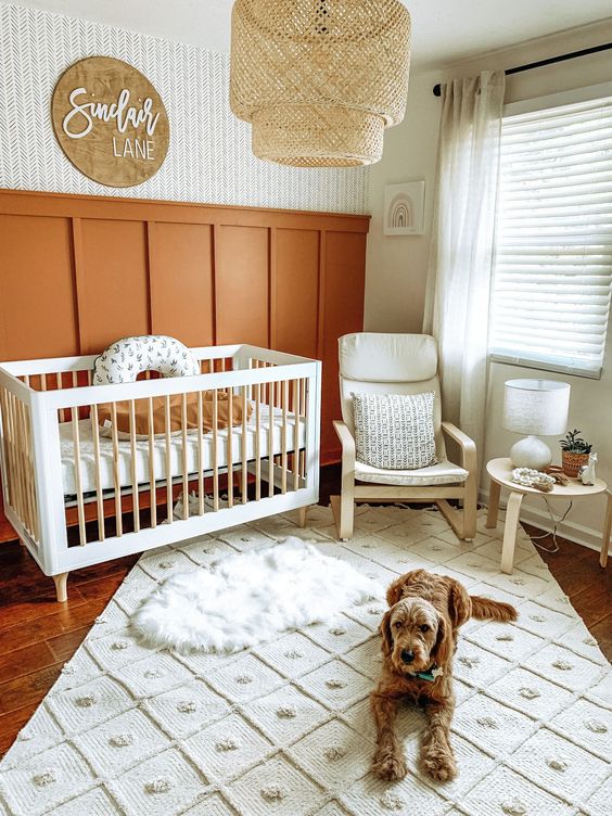 a gender neutral boho nursery with burnt orange paneling, white furniture, a rattan lamp and pretty layered rugs