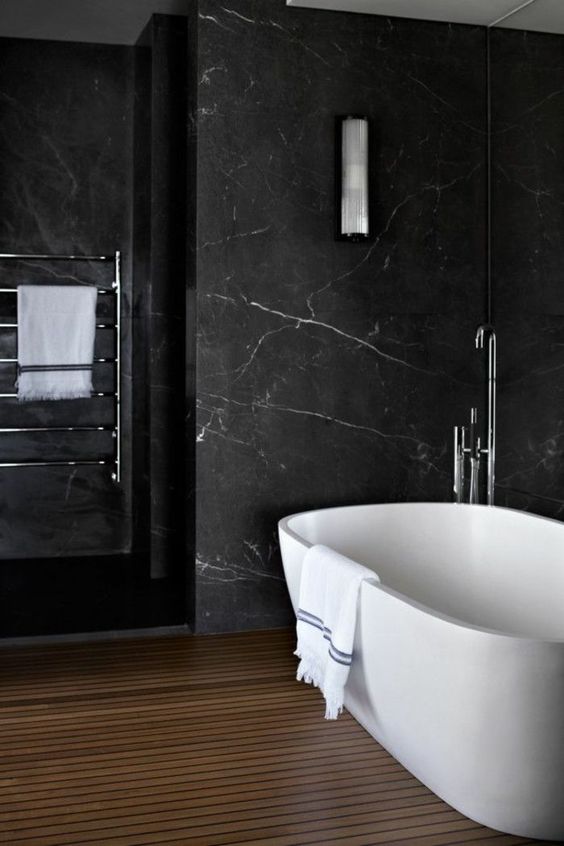 07 a refined bathroom with black marble walls, a wooden slab floor, a pretty tub and neutral fixtures