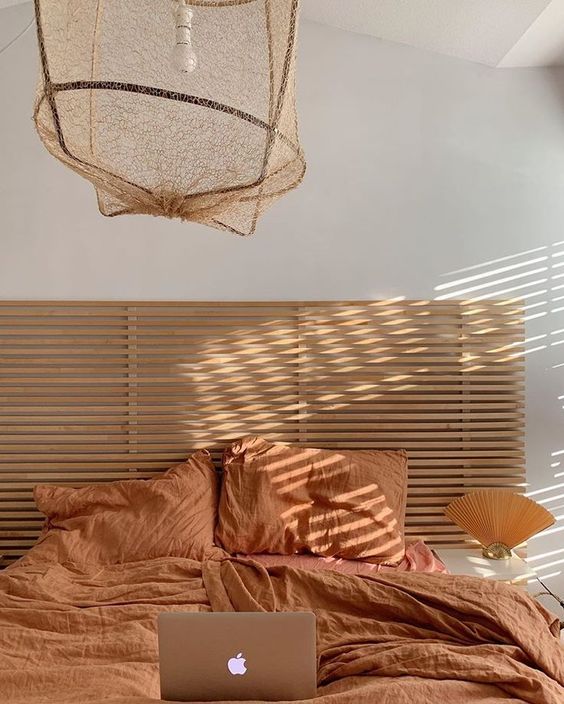 a warm earthy tone bedroom with a light stained bed, a pendant lamp and orange bedding