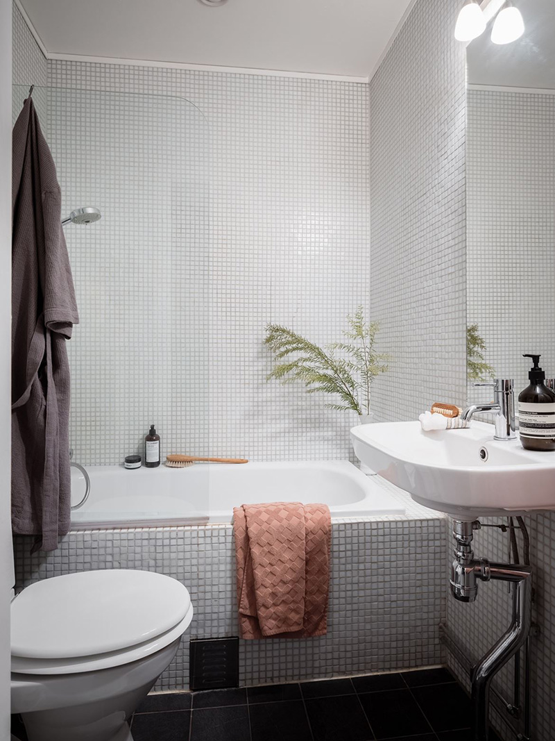 The bathroom is clad with grey textural small scale tiles and white appliances
