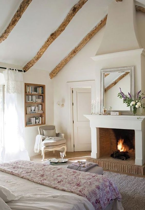 A French chic bedroom with wooden beams, built in shelves, refined furniture and a working fireplace