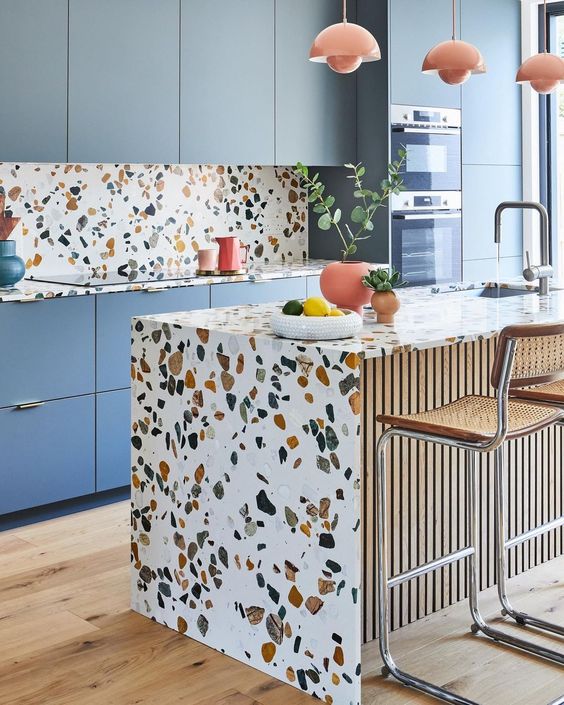 a bright kitchen with blue cabinetry, terrazzo countertops, a backsplash and a kitchen island and coral touches is amazing