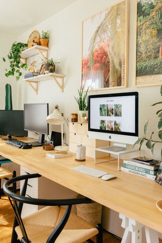 a chic and welcoming home office with a shared desk, woven chairs, bright artworks and potted greenery