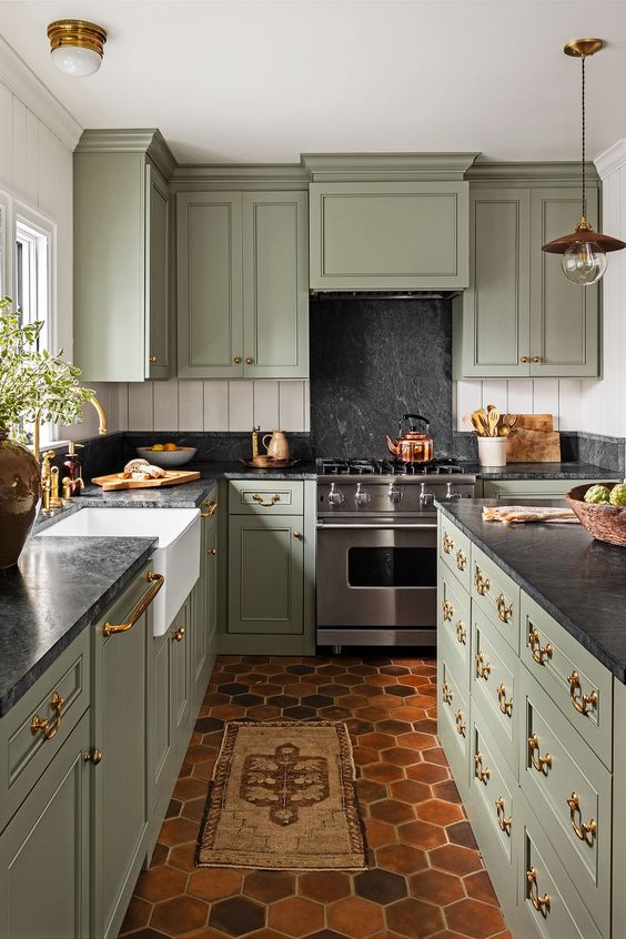 a jaw-dropping sage green vintage kitchen with black stone countertops and a backsplash, with a matching kitchen island and gold handles and fixtures