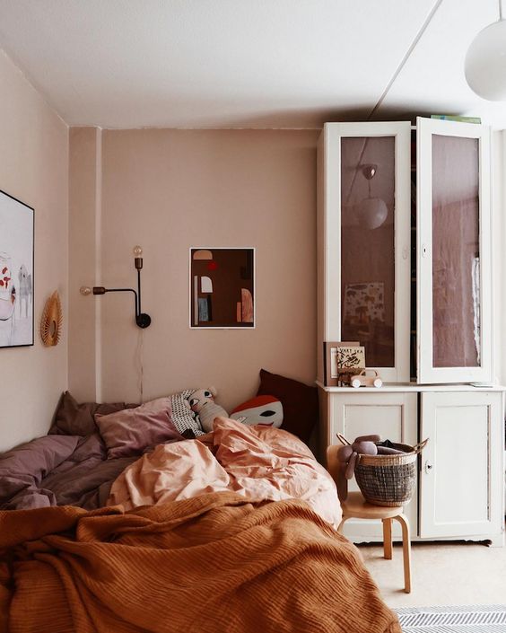 a warm earthy toned bedroom with blush walls, terracotta and blush bedding, wall sconces and a vintage dresser