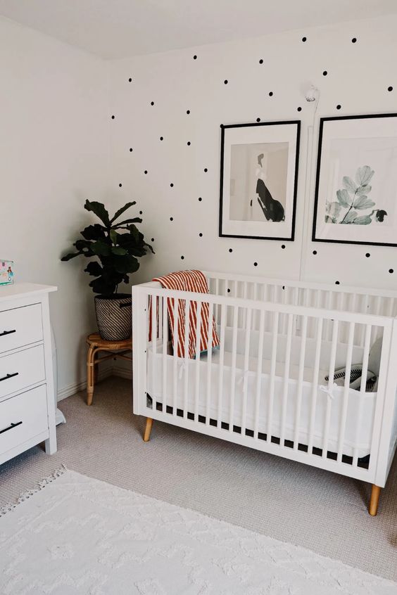 a stylish gender neutral nursery with a polka dot wall, white furniture and a calming gallery wall plus potted plants
