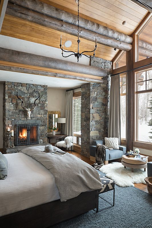 10 a rustic bedroom with wooden logs on the ceiling, a pillar clad with stone and a stone fireplace