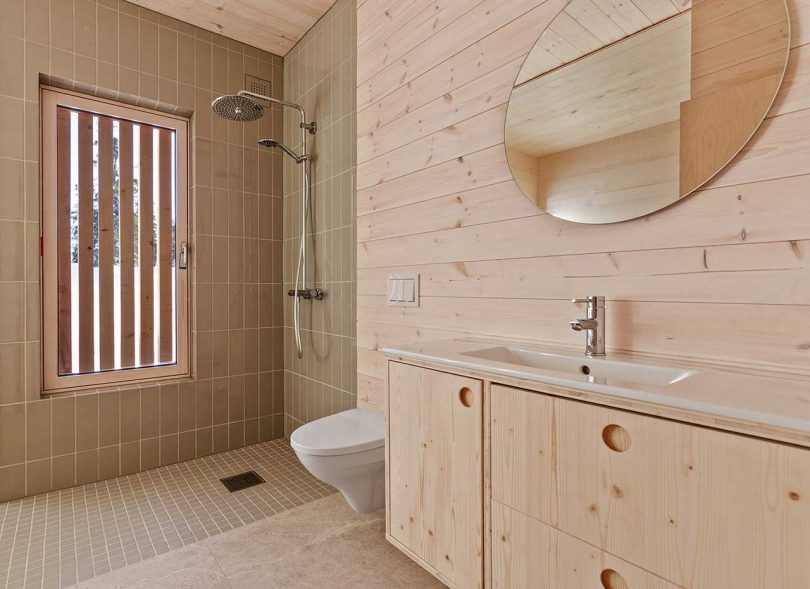 The bathroom is clad with beige tiles and pine wood, it's laconic and simple