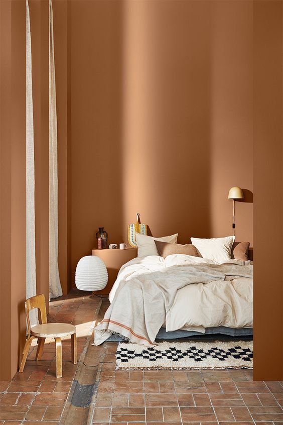 a comforting bedroom with terracotta walls, a brick floor, neutral and terracotta bedding is chic and warm