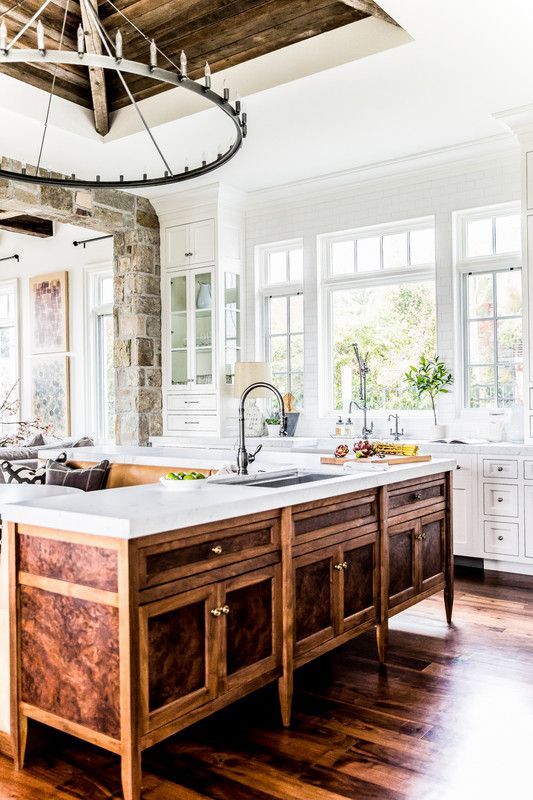 a farmhouse white kitchen with a unique vintage rich-stained wooden kitchen island and a large metal chandelier looks wow