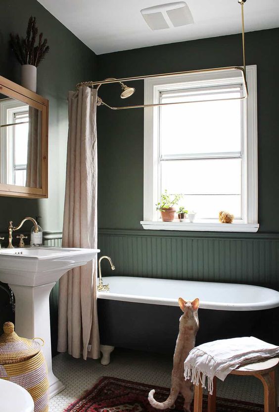 a gorgeous dark green bathroom in vintage style, with a clawfoot tub, a free-standing sink and blush textiles