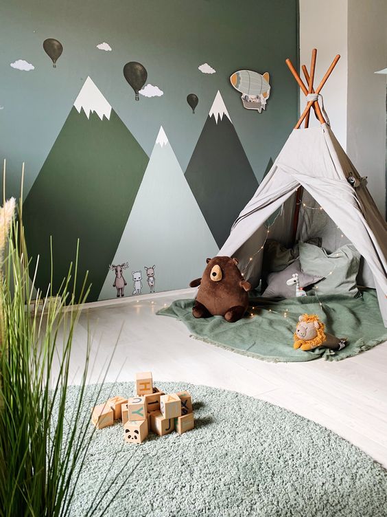 a pretty adventurous nursery with a mountain wall mural, a teepee with lights, green textiles