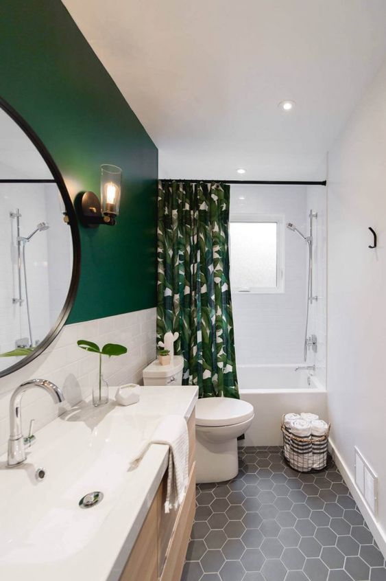 a stylish small bathroom with a green and white tile wall, a grey hex tile floor, white appliances and a tropical print curtain
