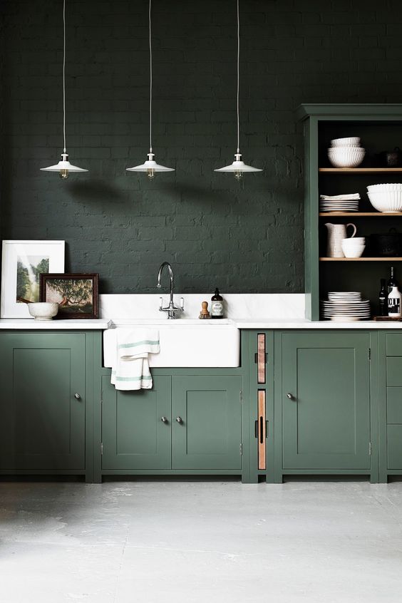 15 a moody hunter green kitchen with vintage cabinets, dark green brick walls, a white stone backsplash and countertops
