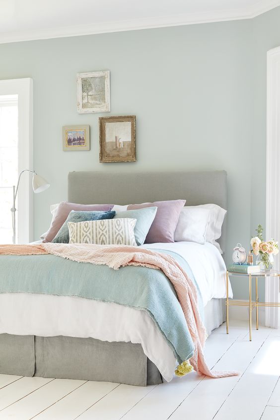 a light blue bedroom with a grey bed, pastel bedding, blooms and a small vintage gallery wall