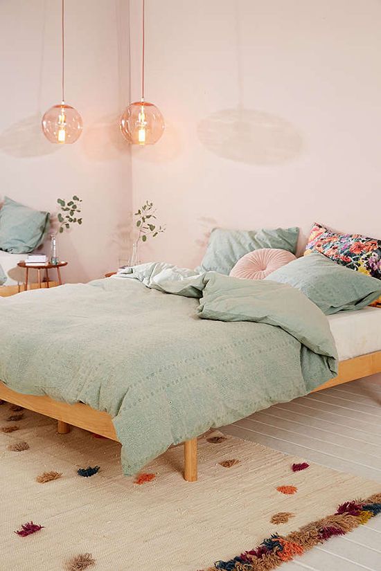 A blush bedroom with wooden furniture, mint colored and pink bedding, pink pendant lamps and a bold rug