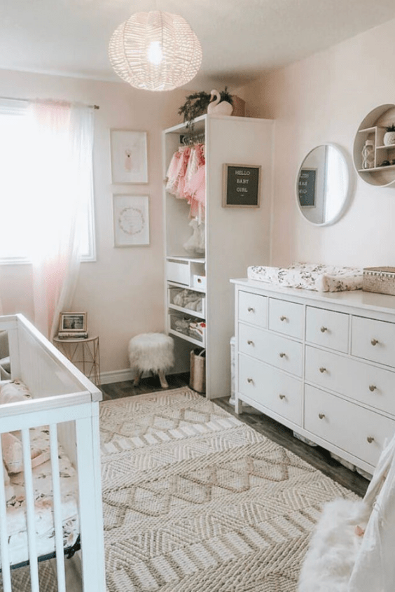 a cozy hygge nursery with blush walls, white furniture, an open wardrobe and a beautiful woven rug