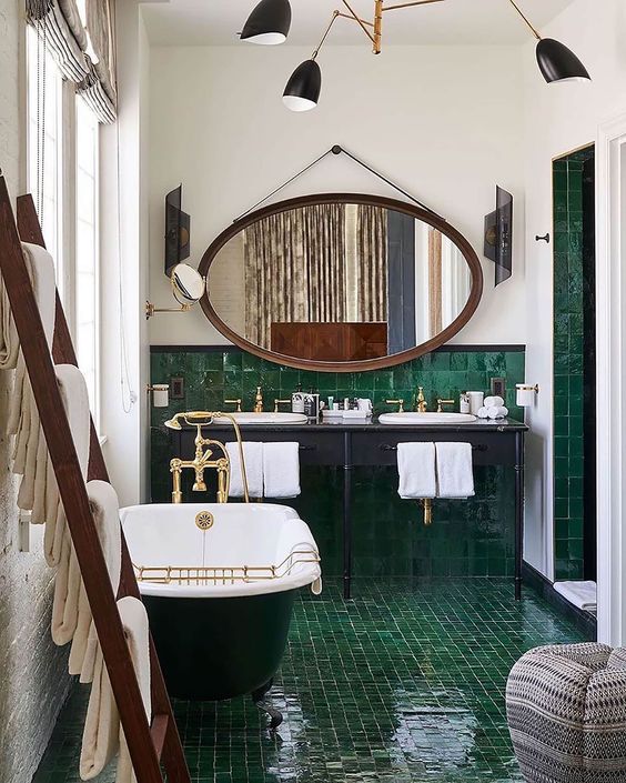 a fantastic 20s bathroom with green glossy tiles, a clawfoot tub, an oval mirror and a shared vanity is very beautiful