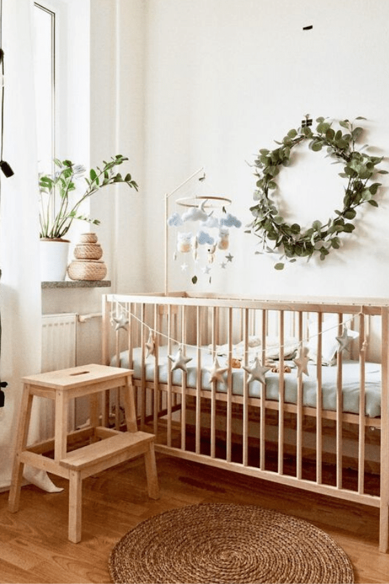 a pretty and welcoming neutral nursery with light stained wooden furniture, pastel bedding and a greenery wreath