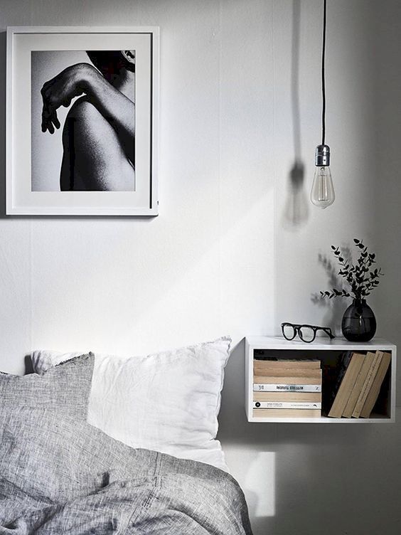 a Scandinavian bedroom with a floating open box nightstand with books and a bulb over the space