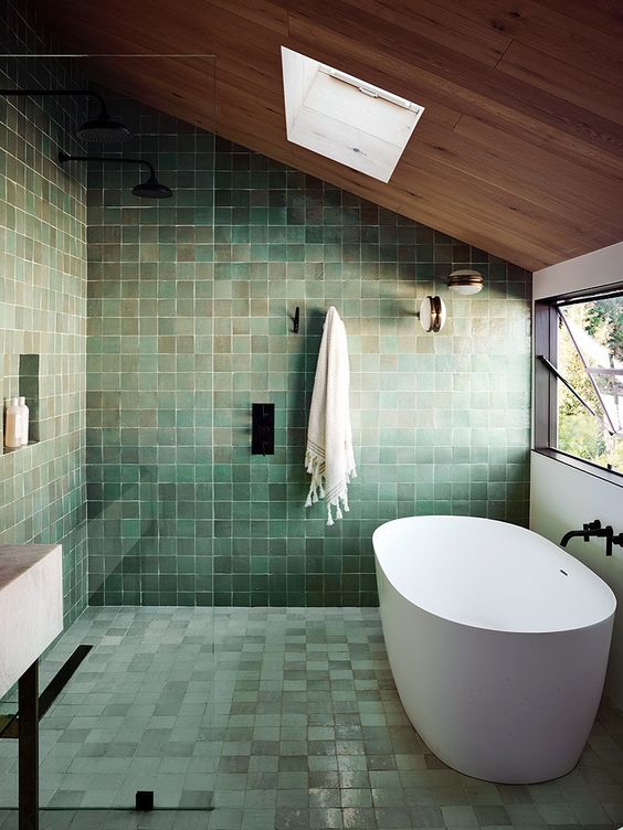 20 a very peaceful green tile bathroom with a wooden ceiling and a skylight, an oval tub and black fixtures