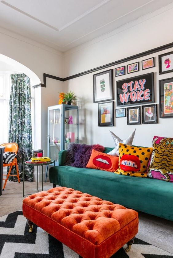 a bold maximalist living room with an orange ottoman, a green sofa, a gallery wall with bold art and colorful pillows