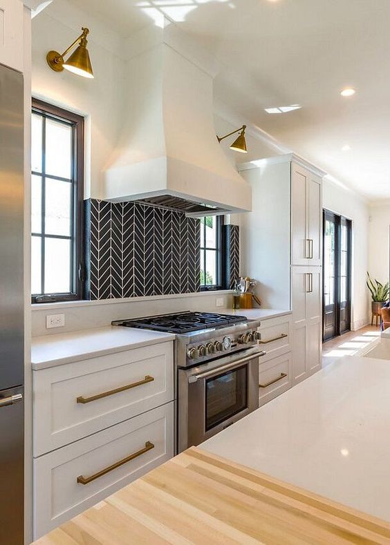 a chic white kitchen with brass handles, wall sconces and a statement black and white geometric tile backsplash