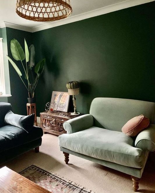 a green on green living room with dark walls, dark and light green furniture, potted plants and a beautiful carved chest