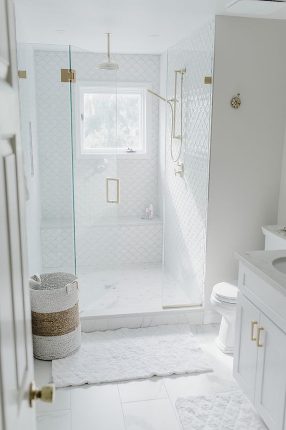 22 a small and chic white bathroom with fish scale tiles and square ones, gold fixtures and a pretty basket for laundry