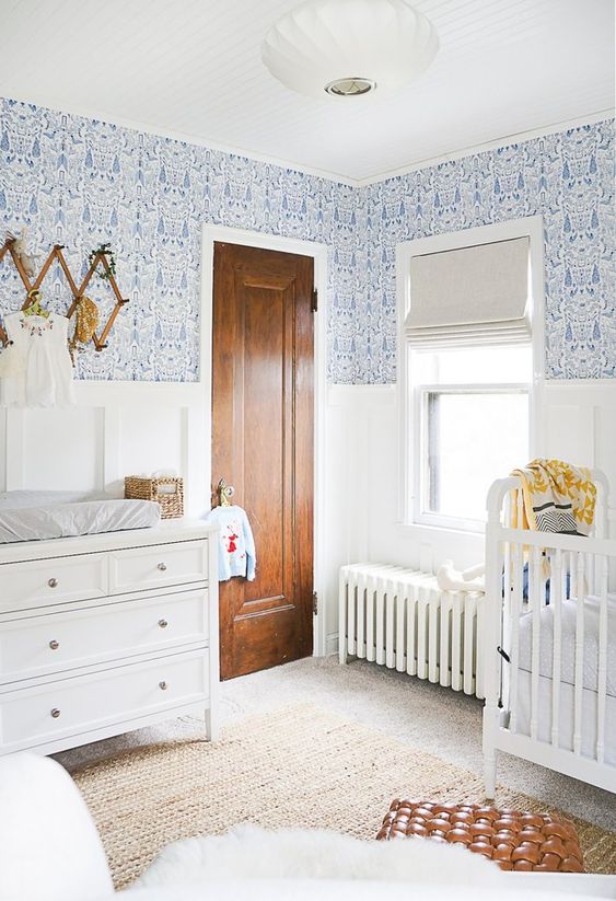 a stylish and beautiful white and blue nursery with printed wallpaper, white furniture and a leather ottoman