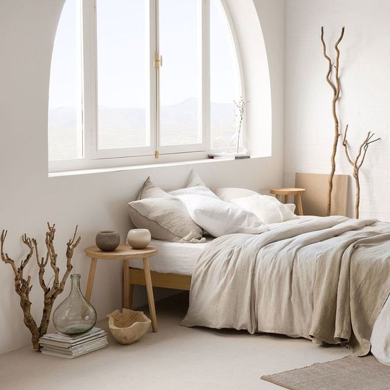 23 a Japandi bedroom with an arched window, light stained wooden furniture, grey and white bedding, driftwood