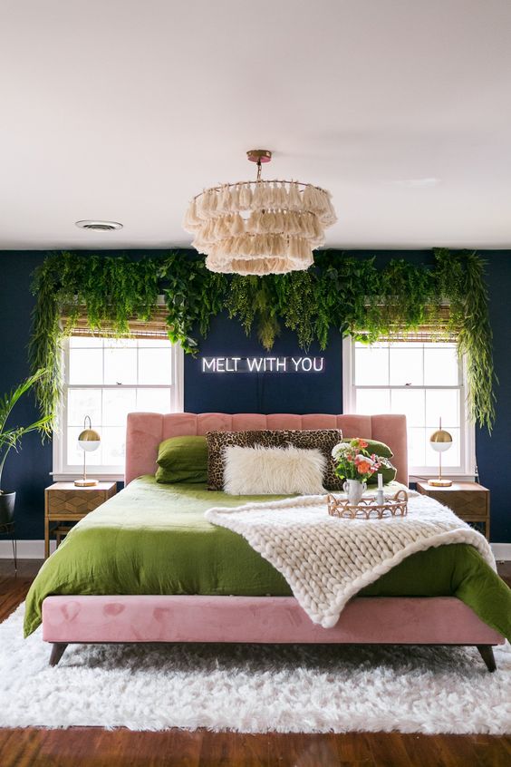 a jaw-dropping teal bedroom with hanging greenery, a pink bed and green bedding and a tassel chandelier