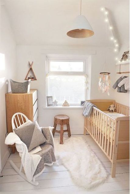 a neutral hygge nursery with light-stained wooden furniture, lights, a crib and a pendant lamp