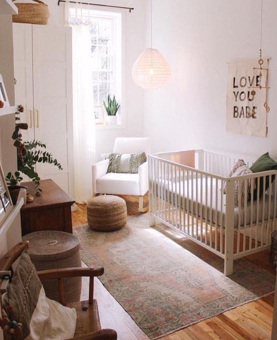 a hygge nursery with white furniture, a jute ottoman and a basket, a pendant lamp and a wooden chair