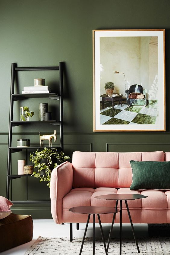 a refined and chic living room with dark green walls softened with pink furniture, catchy tables and potted plants
