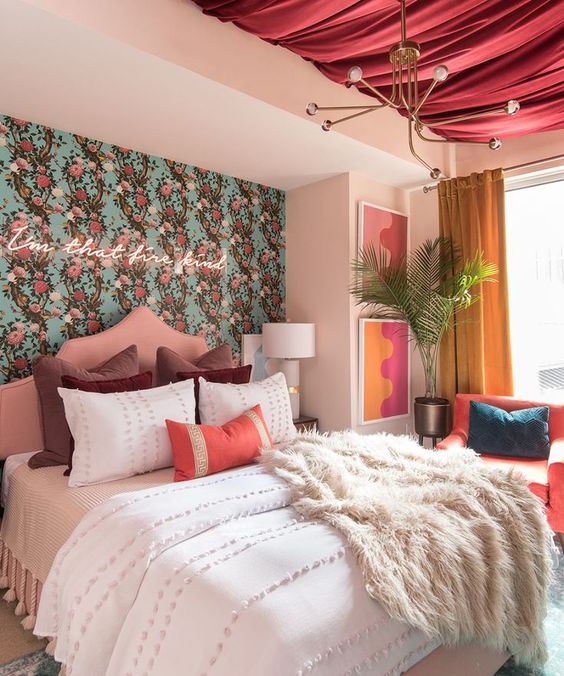 an eye-catchy bedroom with floral wallpaper and a neon sign, a pink draped ceiling, bright textiles and artworks