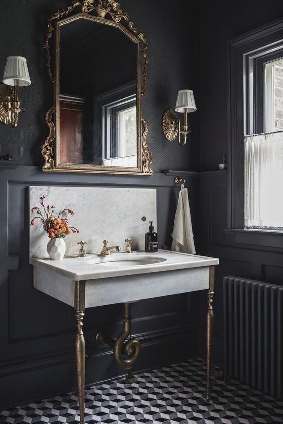 a moody old world bathroom with a diamond print floor, a marble sink, a refined mirror in a gold frame