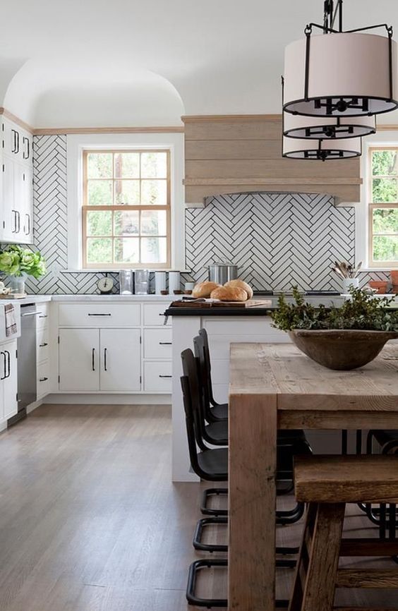 a white kitchen accented with white long tiles and grey grout plus a light-stained wooden hood for more coziness